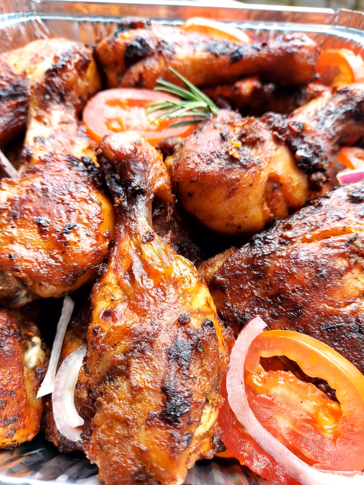Tray of chargrilled marinated chicken pieces with tomato and onion slices