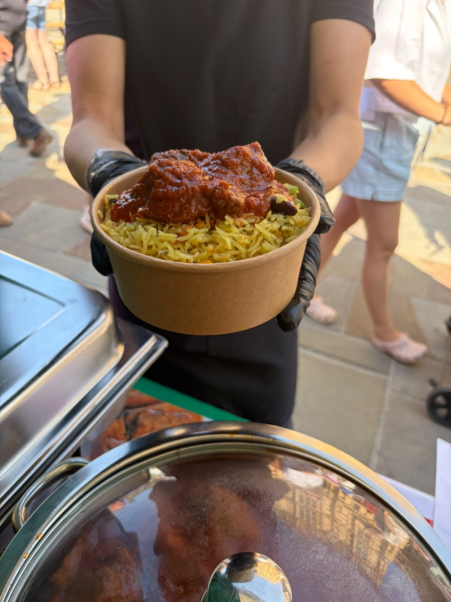 Bowl of Nigerian fried rice topped with spicy chicken at an event