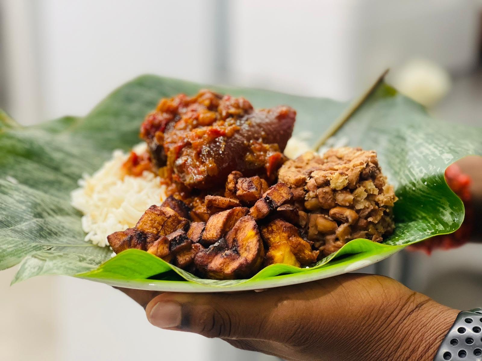 Banana leaf plate of white rice, stewed meat, fried plantain and moin-moin