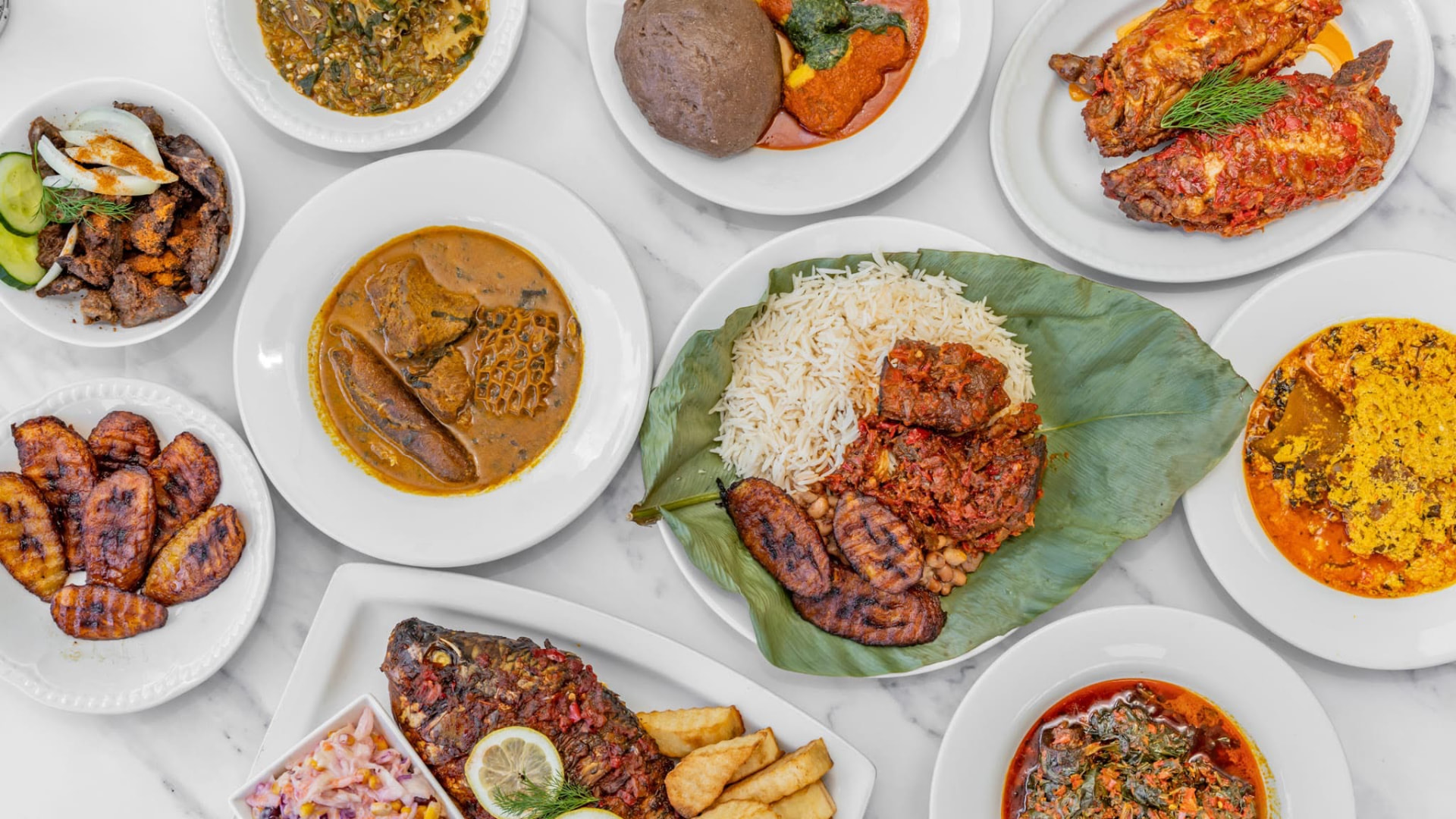 Overhead spread of Nigerian dishes: native soups with swallow, jollof rice, suya, grilled fish and fried plantain