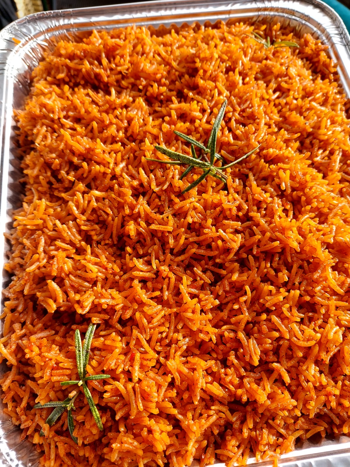 Large catering tray of smokey party jollof rice garnished with rosemary