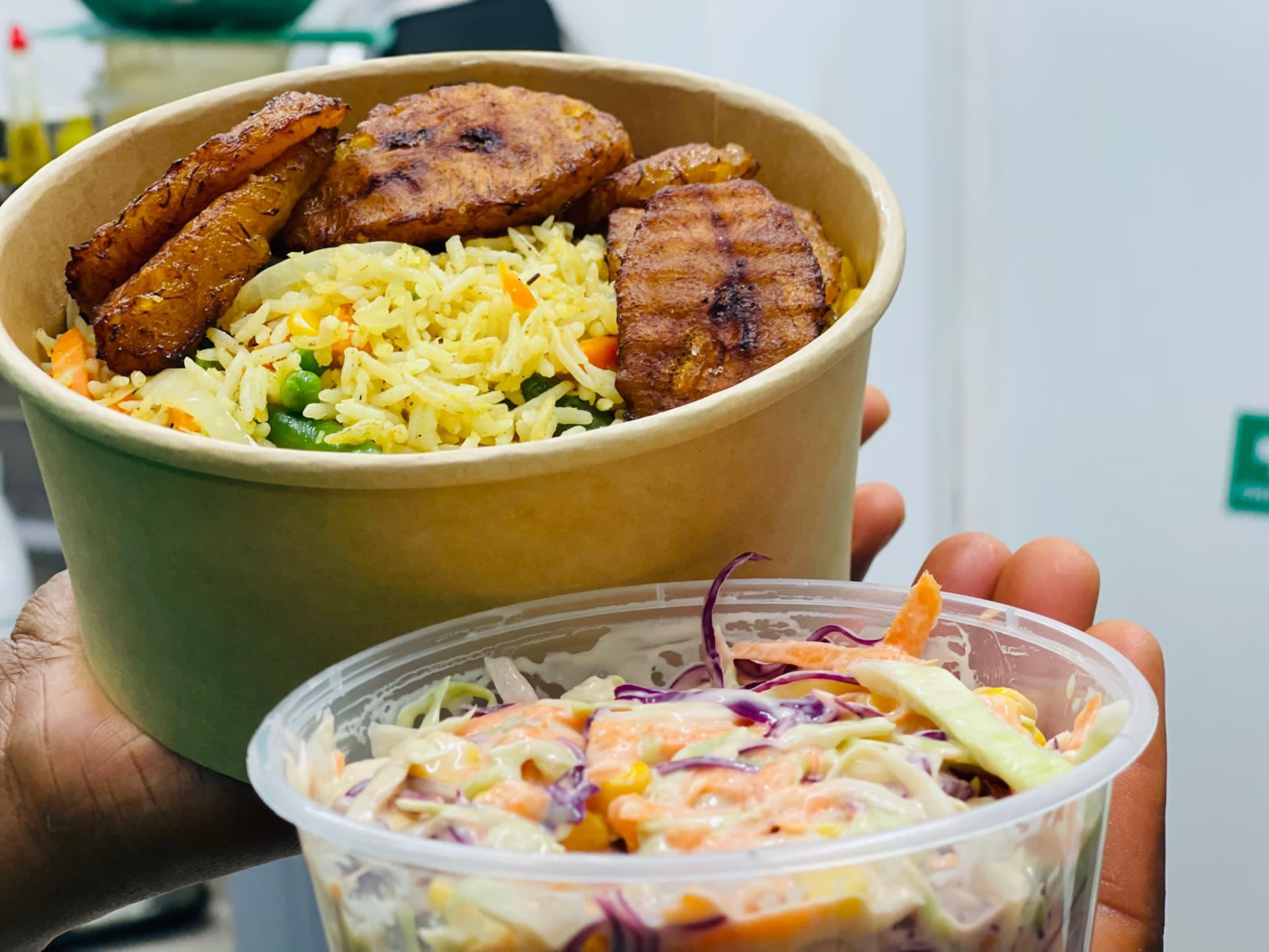 Takeaway bowl of fried rice with fried plantain and a pot of coleslaw